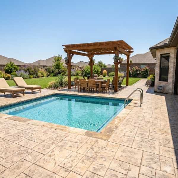 A custom stamped concrete pool deck and patio featuring a tan ashlar slate pattern, a wooden pergola with a dining set, and professional landscaping in Amarillo, Texas.